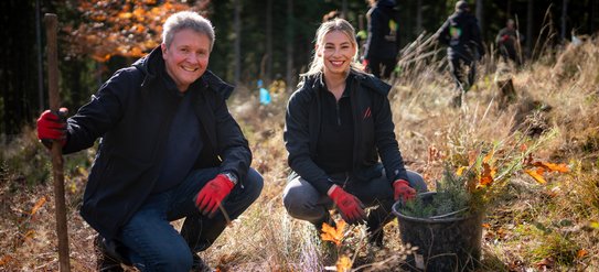 Zwei Personen hockend im Wald mit Blick zur Kamera