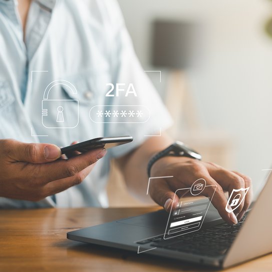 Eine Person hält ein Smartphone in der Hand, während sie einen Laptop bedient. Smartphone-Schutz mit Zwei-Faktor-Authentifizierung, Cybersicherheit und Datenschutz Daten schützen. 