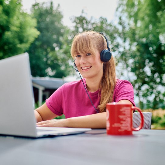 Frau sitzt mit ihrem Laptop im Home Office im Garten mit einem Headset