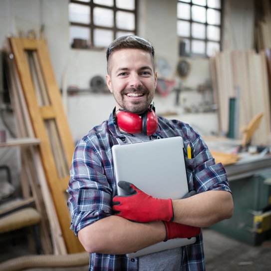 Ein Handwerker in seiner Werkstatt, der seinen Laptop in den Armen hält