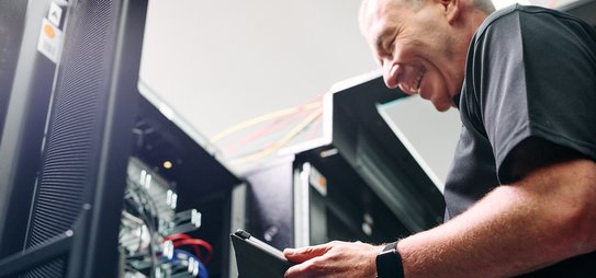Ein Mann steht vor einem geöffneten Serverturm mit einem Tablet in seiner Hand
