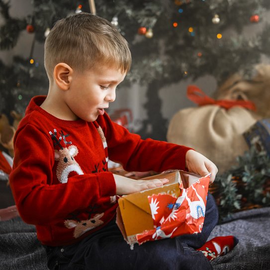 Ein kleines Kind öffnet vor dem Weihnachtsbaum sitzen ein Weihnachtsgeschenk