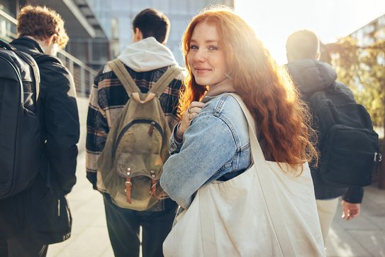 Ein Mädchen läuft hinter einer Gruppe Jugendlicher und schaut lächelnd in die Kamera über ihre Schulter