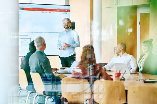 Ein Mitarbeitender präsentiert in einem Meeting vor weiteren Personen.